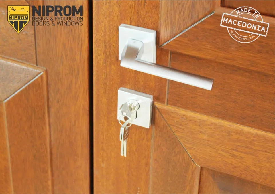Close-up of a warm wood-tone door with an aluminium lever and a key in the lock