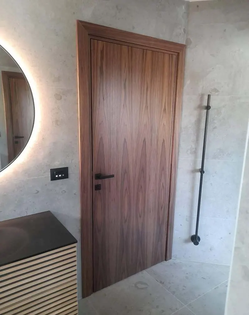 Installed flush walnut-veneer door in a bathroom with a lit mirror